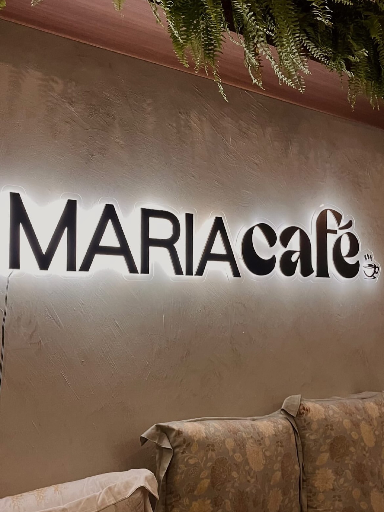 Letreiro iluminado com o nome Maria Café na parede do salão